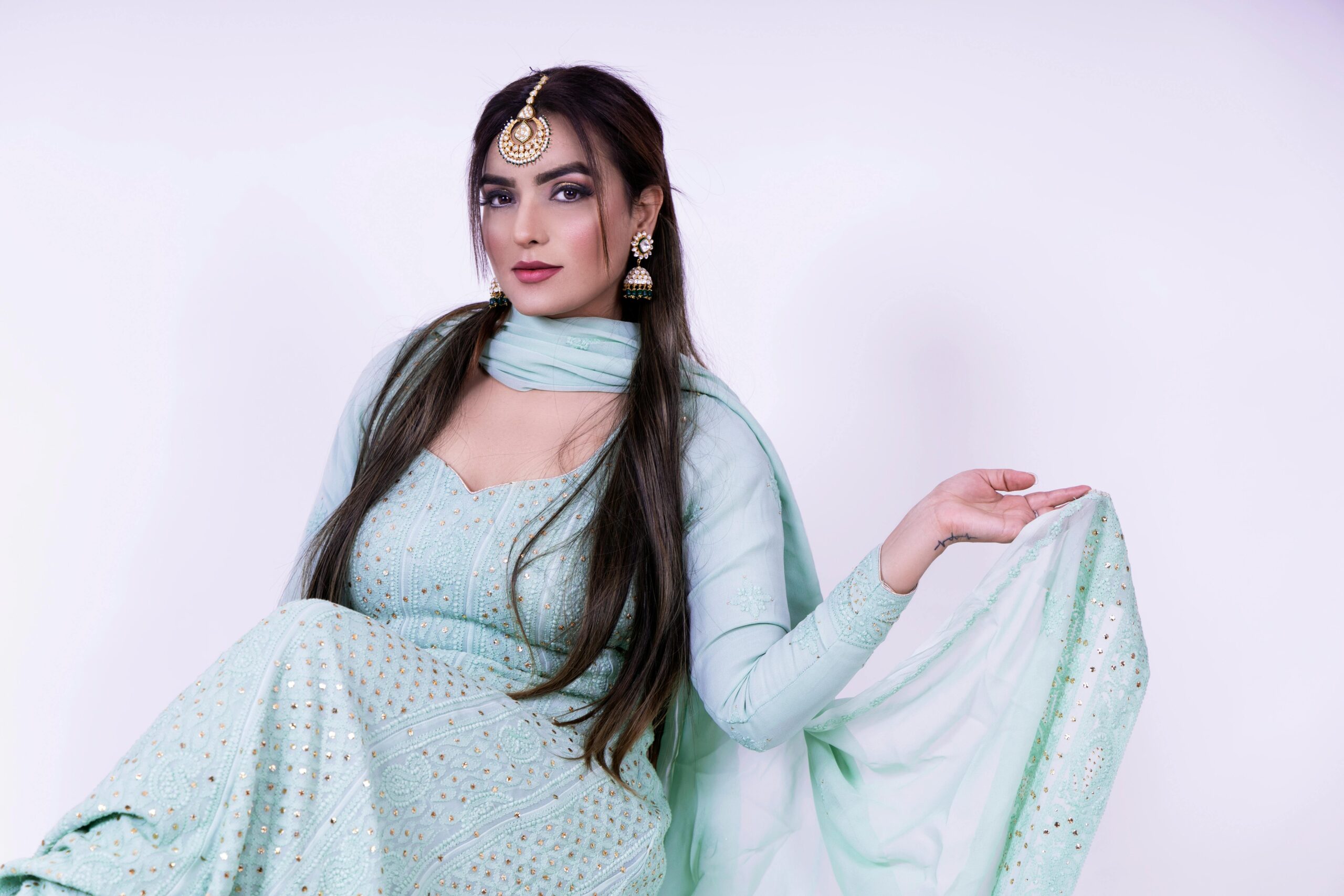 A young woman poses elegantly in a mint green saree adorned with traditional jewelry, showcasing cultural elegance.